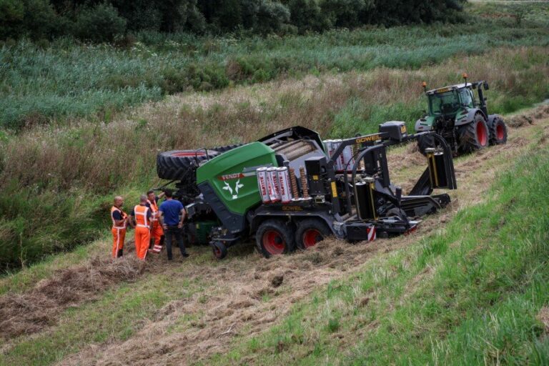 Tractorbestuurder met balenpers van de dijk gereden